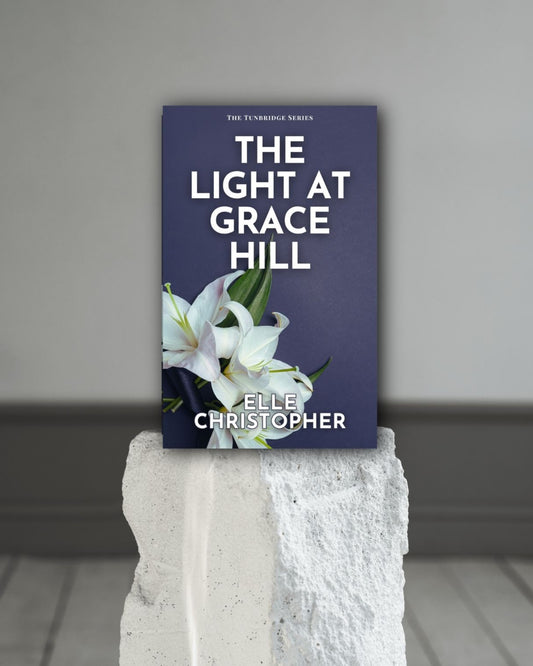 Book titled 'The Light at Grace Hill' by Elle Christopher on a white pedestal against a gray background